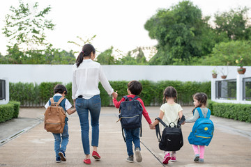 Group of preschool student and teacher holding hands and walking to home. Mom bring her children go to school together. Back to school and Education concept. People and lifestyles theme. Back view