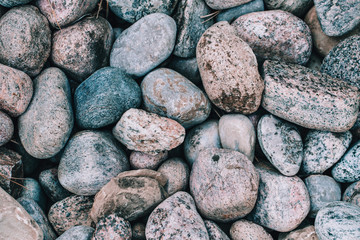 Closeup of big huge large grey pink blue stones rocks pebbles lying on ground. Natural environmental background texture. Toned with modern hipster film filters.
