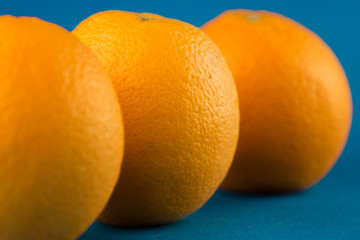 Closeup of a horizontal row of three vibrant orange oranges on light blue background