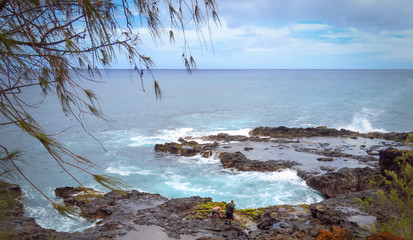 Panoramic landscape of two men looking for crabs at the rocky shore near Spouting Horn blowhole, Pacific Ocean, Kauai, Hawaii, USA