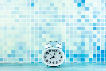 white alarm clock front a blue tile wall.