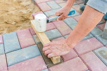Worker laying red and gray concrete paving blocks. Road Paving, construction.