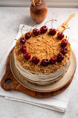 honey cake with cherries on top on a brown plate, on a light marble backdrop