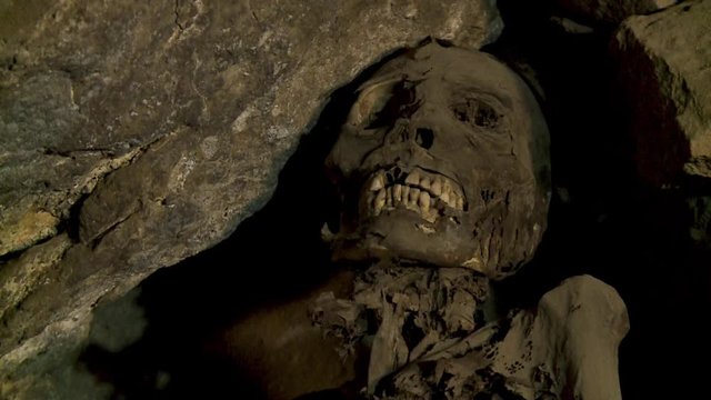 Close-up low-angle portrait still shot of a pre-Incan mummy with a laughing face inside a rocky cave tomb at Coquesa historic cemetery museum, Uyuni, Bolivia