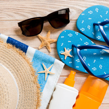 flip flops, straw hat, starfish, sunscreen bottle, body lotion spray on wooden background top view . flat lay summer beach sea accessories background, holiday concept