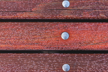 Red boards near the bench are covered with hoarfrost with iron bolts.
