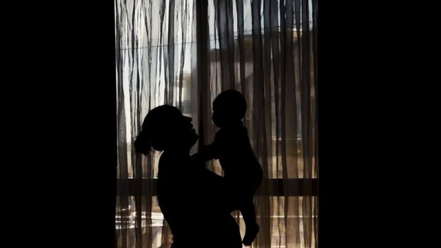 silhouette of pregnant mother and six months old baby - mother lifting kissing and spining little baby