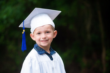 Cute smiling boy in cap and gown after kindergarten graduation