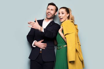 Joyful couple, elegantly dressed, standing on a blue background