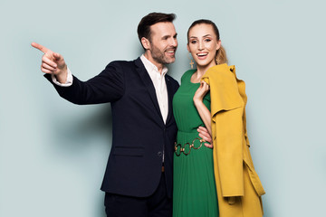 Joyful couple, elegantly dressed, standing on a blue background