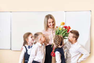 Beautiful children-students together in class at school give flowers to their best woman teacher