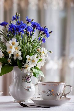 On the table is a cup of tea and a bouquet of wild flowers in a vase