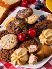 Chocolate oatmeal cookies and sand heart shape cake with blueberries on table in farm style. Table setting breakfast on gingham tablecloth. Homemade, delicious recipes.