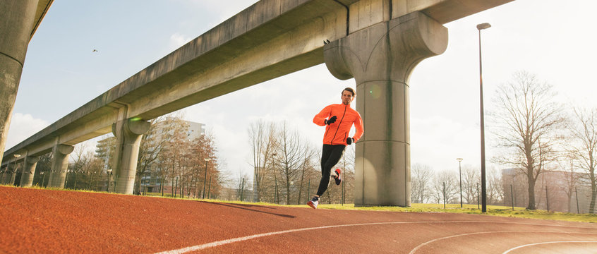 A male runner or athlete running on a urban running track.