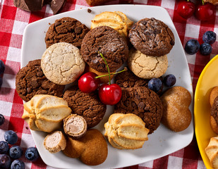Oatmeal Cookies and sand chocolate cake with blueberries on wooden table with gingham cloth in farm style close up. Table setting breakfast for two with cups in. Perfect product.