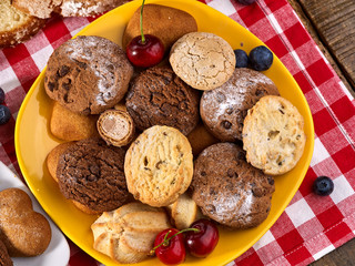 Oatmeal Cookies and sand chocolate cake with blueberries on wooden table with gingham cloth in farm style close up. Table setting breakfast for two with cups in. Best selection of confectionery
