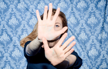 Blonde girl showing stop sign at camera over blue background.