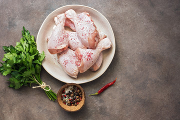 Chicken uncooked drumstick on a plate, dark brown rustic background. Flat lay, overhead view, copy space.