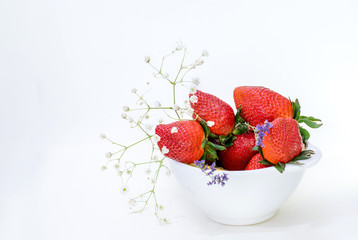 white bowl full of strawberries decorated with flowers on white background