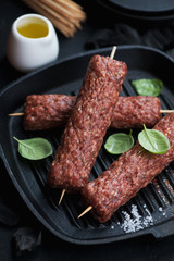 Cast-iron grill pan with raw kebabs made of marbled beef meat on skewers, closeup, vertical shot