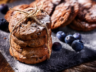 Serving food on slate onto wooden table. Oatmeal cookies biscuit with blueberry on picnic dark tiles countrylike. Chocolate chip cookies tied with string. Best range of confectionery products.