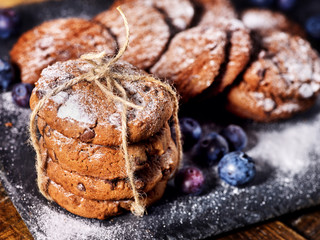 Serving food on slate onto wooden table. Oatmeal cookies biscuit with blueberry on picnic dark tiles countrylike. Chocolate chip cookies tied with string. How and from what make sweets.