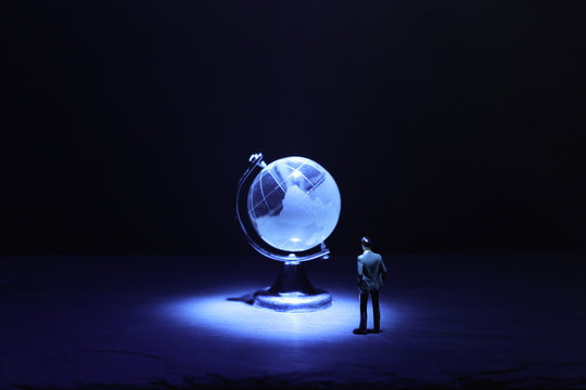 Miniature man looking at Small crystal globe in front of dark and dramatic light.global issues concept