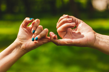 Closeup shot of hands making a pinkie promise sign in nature – Mother and daughter crossing their little fingers in symbol of commitment - obrazy, fototapety, plakaty