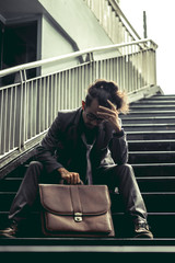 Man in suit are stressed because he is unemployed. He sit at the stairs in the city with despair.