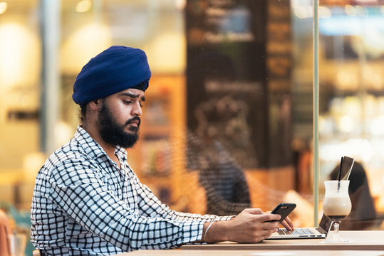 Young bearded indian man using smartphone and laptop