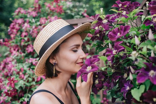 Profile portrait of young female enjoying the scent of violet flowers in the garden with closed eyes