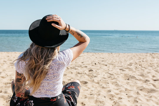 Young blonde woman sitting on the beach facing the water