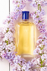 Obraz na płótnie Canvas yellow bottle of women's perfume with lilac flowers on white wooden background