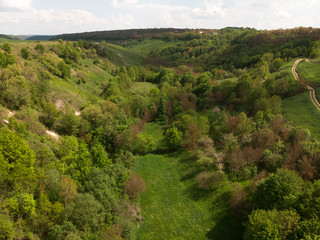 Fototapeta na wymiar Aerial view of a countryside canyone, with dirt road and green summer hill by drone, beautiful nature concept design