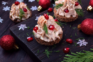Canape shaped as a Christmas tree with pate garnished with pomegranate and dill surrounded by Christmas decorations