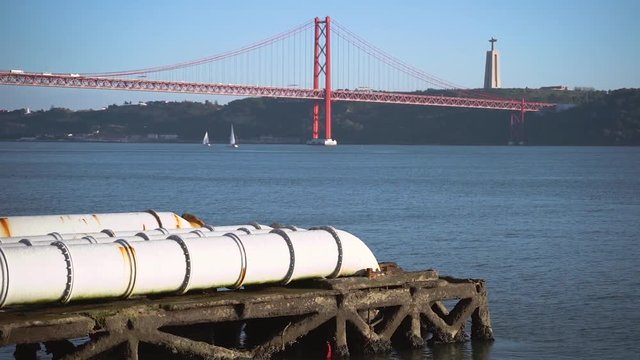 Industrial white pipes near Tejo power station in Lisbon, feeding into the tagus river, Christ King and Bridge in the background, Portugal