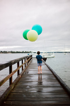 Boy on a jetty with three large helium filled balloons on string