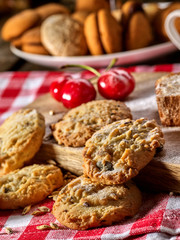 Oatmeal cookies and cherry on kitchen cutting board gingham checkered cotton fabric on table in village style for picnic with plate of macaron background. Exhibition of culinary works.