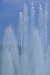 Splashing water from a fountain close up against the blue sky.