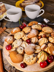 Oatmeal cookies and sand chocolate cake with cherry on cutting board on wooden table in rustic style served with cups and dessert spoons. It has pleasant taste.