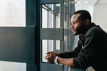 Young black man with pensive expression looking out window