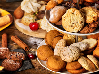 Oatmeal and nut cookies and sand biscuit on tier cake stand , crispy wafer rolls with cream on kitchen on wooden table in rustic natural style. Perfect for breakfast.