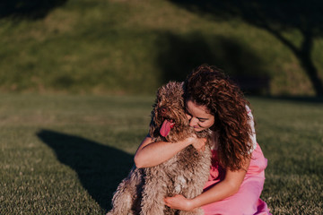 young owner woman with her brown spanish water dog having fun outdoors in a park at sunset. love for animals concept