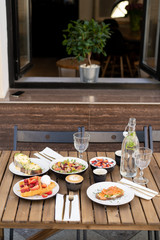 Stunning breakfast or lunch in open air in a cozy summer cafe. Poached eggs with Dutch sauce and avacado, coffee, bottle of water with mint, granola with fruit, waffles with ice cream, salad and chia 