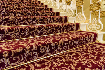 Brass stairrods holding down red patterened Axminster carpet on the stairs of a posh house.