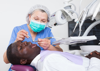 Dentist is treating male patient which is sitting in dental chair