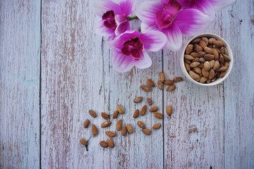 Almonds nuts in bowl with a pink orchid flower on blue wood background, top view