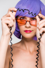 woman in purple wig looking at cord of vintage telephone, isolated on grey