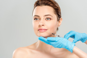 cropped view of cosmetologist in blue latex gloves holding syringe near face of naked woman isolated on grey
