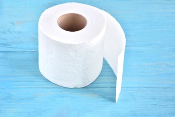 A roll of soft white toilet paper with selective focus on textured wooden background. Restroom concept with toilet paper on blue wood backdrop. Daily hygiene cleanser. Recycling toilet paper. 